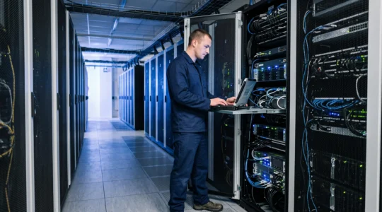 Technicien cybersécurité intervenant sur un serveur dans une allée de data center moderne avec rangées de racks et éclairage technique
